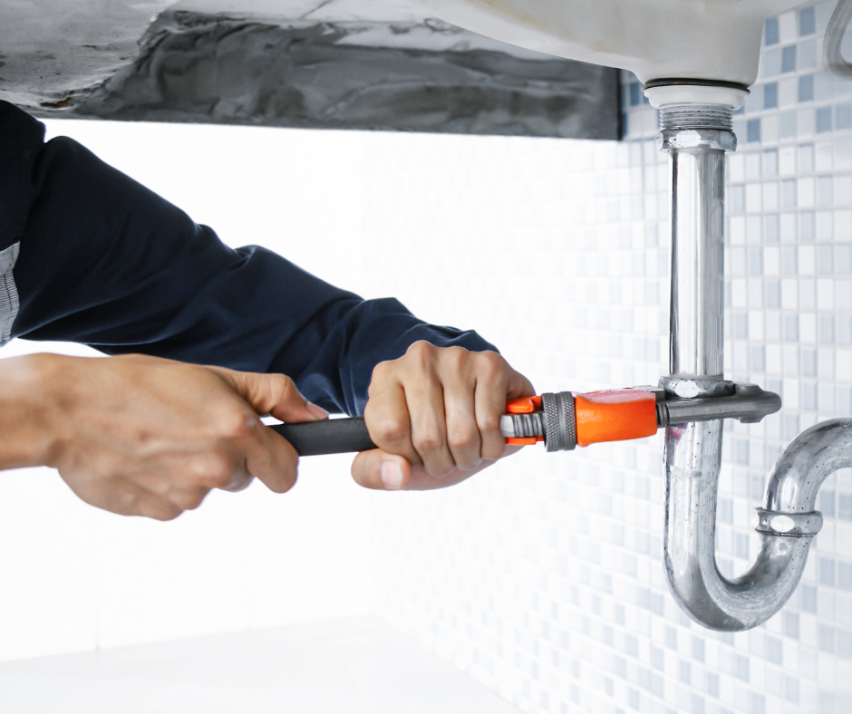 A plumber uses a wrench on a pipe under a sink